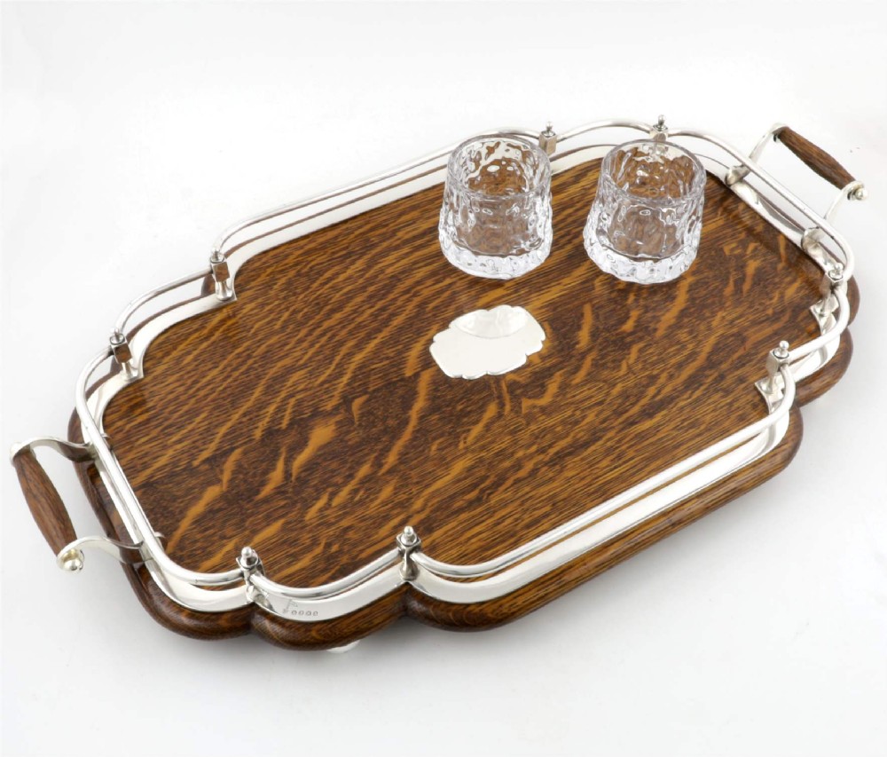 A late Victorian shaped English oak serving tray featuring a silver-plated raised gallery rail, twin wood-mounted handles, and a central blank silver cartouche. View XII