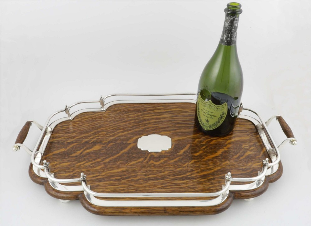 A late Victorian shaped English oak serving tray featuring a silver-plated raised gallery rail, twin wood-mounted handles, and a central blank silver cartouche. View XIV