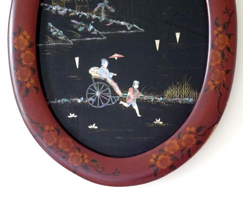 fig 1. An oval red-lacquered framed artwork depicting a Japanese scene with Mount Fuji and a rickshaw in mother-of-pearl and abalone shell inlay against a black background.