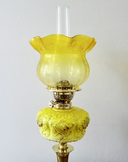 fig 1. A late Victorian oil lamp featuring a yellow glass frilled shade, a moulded yellow glass reservoir, a turned brass pedestal base, and a tall clear glass chimney.
