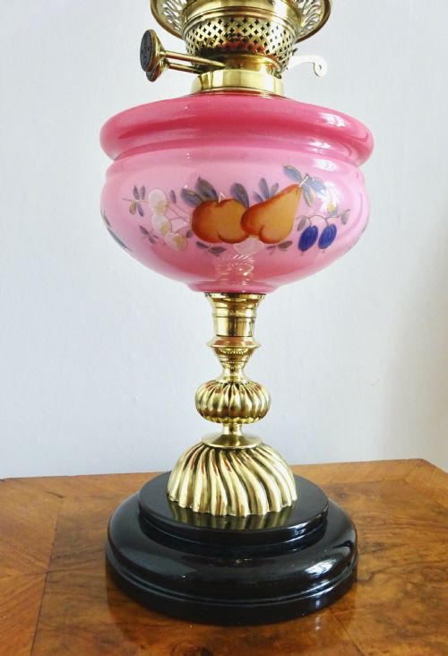 fig 1. An early twentieth-century brass oil lamp featuring a pink hand-painted glass reservoir, an etched floral glass globe shade, a clear glass chimney, and a black stepped base.