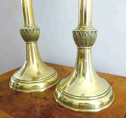 fig 1. A pair of tall, polished brass candlesticks featuring turned shafts, carved leaf motif knops, circular bases, and wide upper sconces.