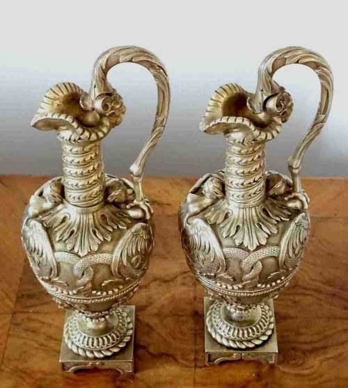fig 1. A pair of ornate Victorian bronze ewers featuring high-relief classical carvings, scrolling handles, and square pedestal bases.