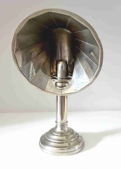fig 1. A nickel-plated antique candle lamp featuring a stepped circular base, tubular stem, and a curved fan-like reflector hood attached near the candle nozzle.