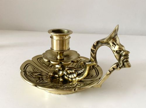 fig 2. An antique French brass chamberstick featuring a scalloped tray base, turned candle socket, and a cast handle shaped like a grotesque face.