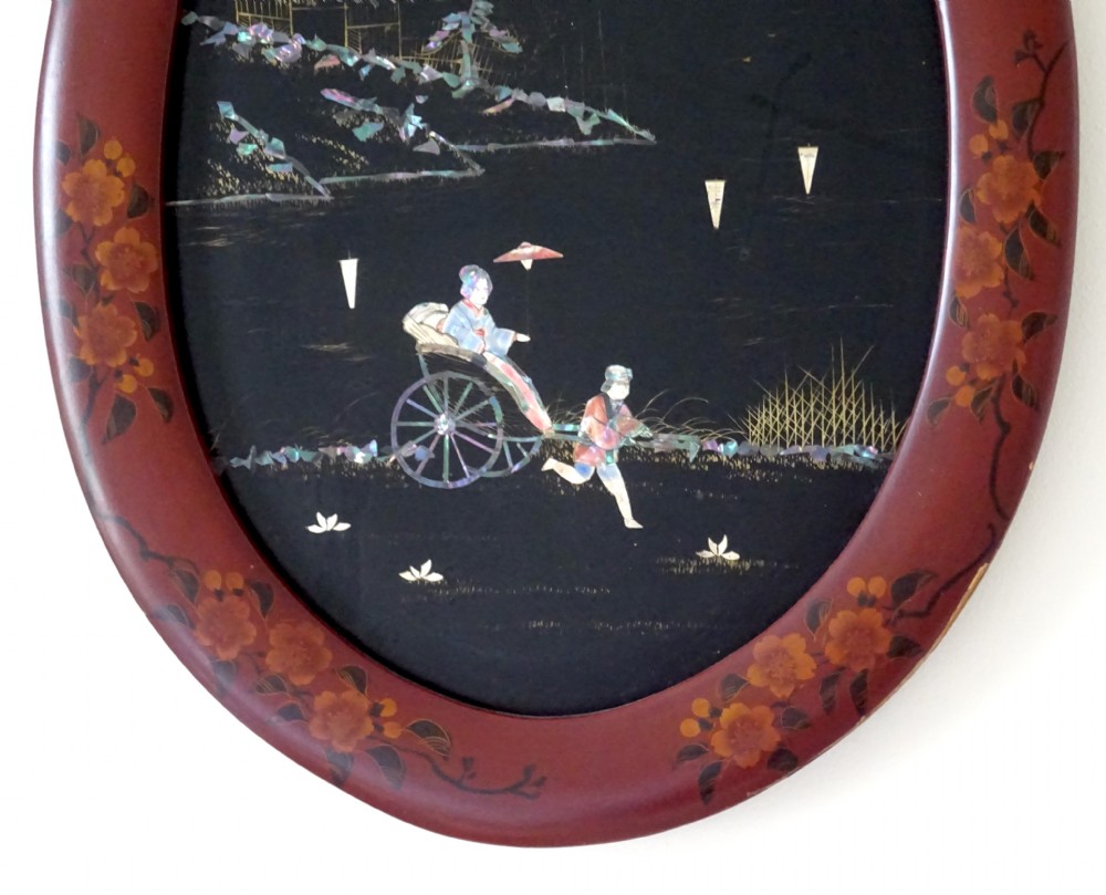 An oval red-lacquered framed artwork depicting a Japanese scene with Mount Fuji and a rickshaw in mother-of-pearl and abalone shell inlay against a black background. View II