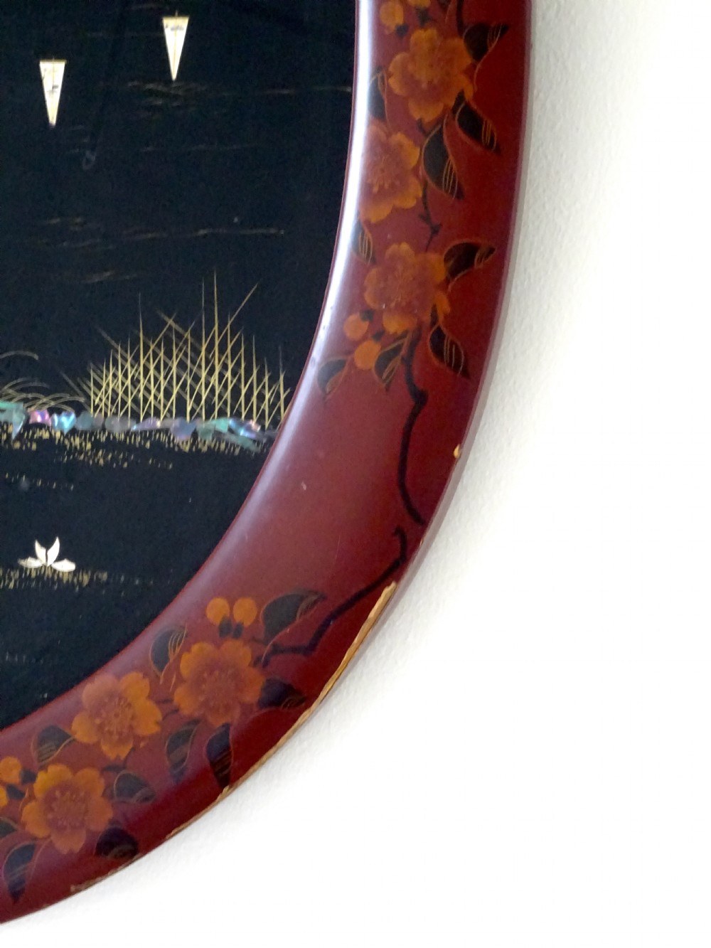 An oval red-lacquered framed artwork depicting a Japanese scene with Mount Fuji and a rickshaw in mother-of-pearl and abalone shell inlay against a black background. View III
