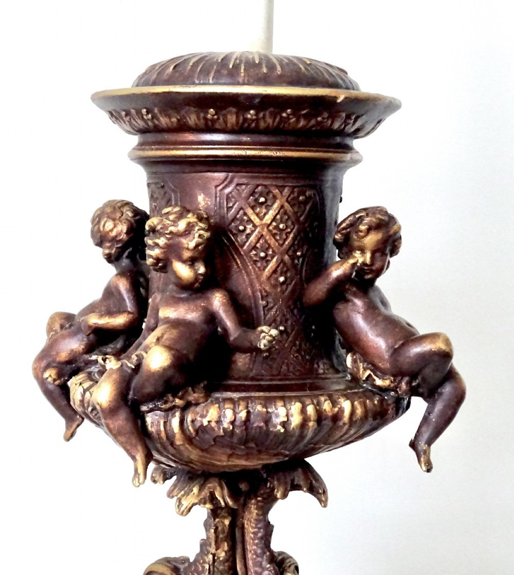 A cast metal Neoclassical table lamp base featuring sculpted cherubs and dolphin motifs mounted on a round onyx plinth. View II