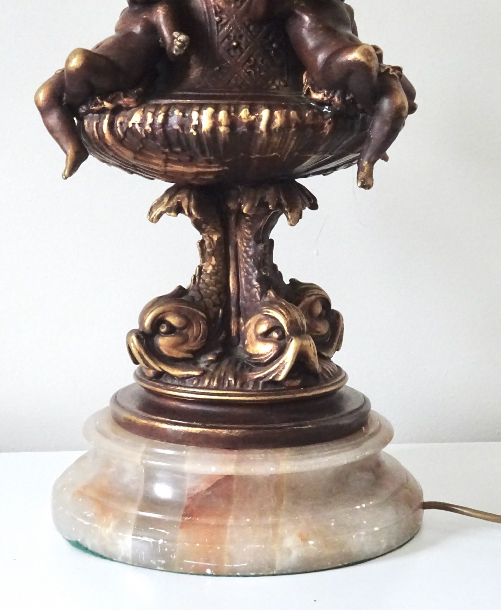 A cast metal Neoclassical table lamp base featuring sculpted cherubs and dolphin motifs mounted on a round onyx plinth. View V