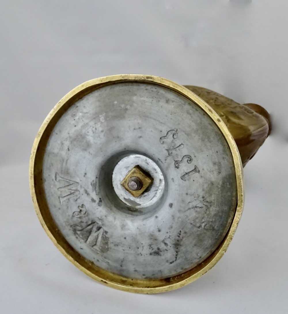 An ornate late Victorian brass oil lamp featuring a weighted circular base, central stem, detailed reservoir with relief carving, and a top carrying ring handle. View X