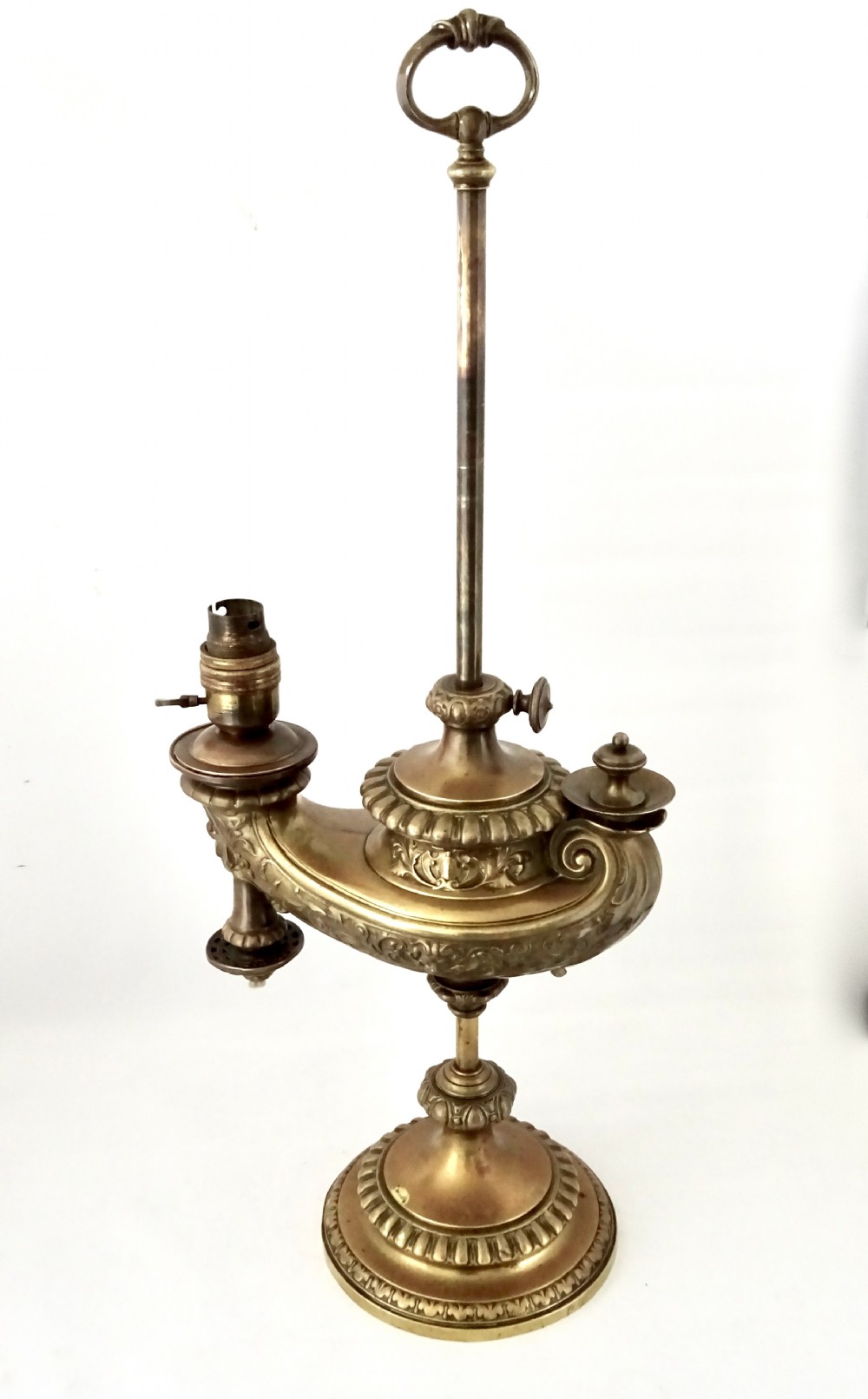 An ornate late Victorian brass oil lamp featuring a weighted circular base, central stem, detailed reservoir with relief carving, and a top carrying ring handle. View IX