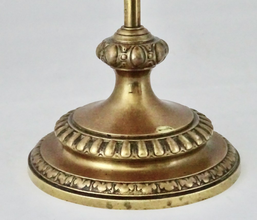 An ornate late Victorian brass oil lamp featuring a weighted circular base, central stem, detailed reservoir with relief carving, and a top carrying ring handle. View VI