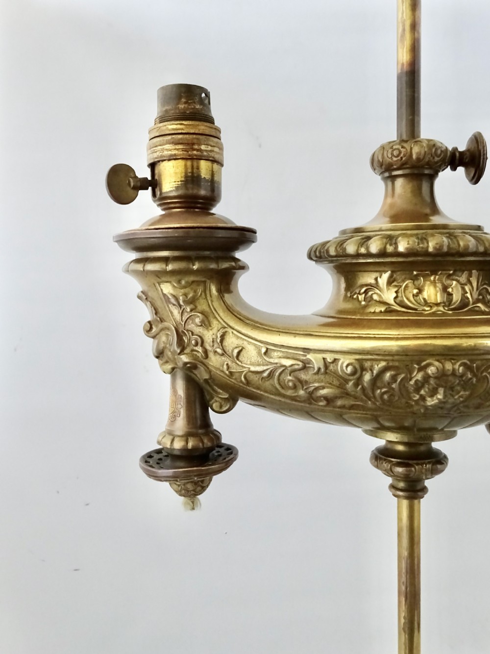 An ornate late Victorian brass oil lamp featuring a weighted circular base, central stem, detailed reservoir with relief carving, and a top carrying ring handle. View VII