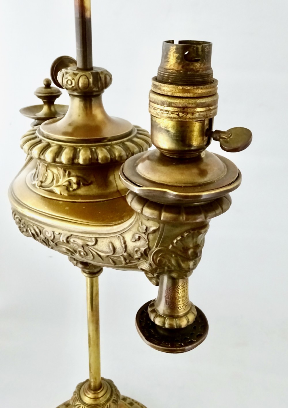 An ornate late Victorian brass oil lamp featuring a weighted circular base, central stem, detailed reservoir with relief carving, and a top carrying ring handle. View III