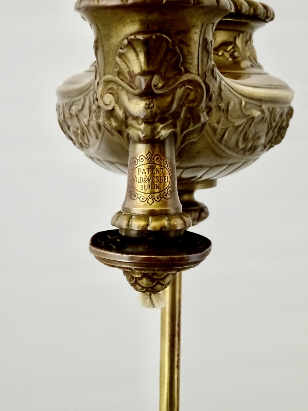 An ornate late Victorian brass oil lamp featuring a weighted circular base, central stem, detailed reservoir with relief carving, and a top carrying ring handle. View IV