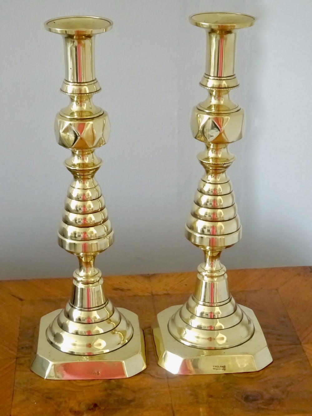 A pair of tall turned brass candlesticks featuring beehive stems, diamond knops, and square bases with canted corners.