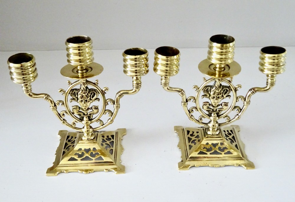 A pair of cast brass three-light candelabras featuring central grotesque mask motifs and pierced square bases. View IV