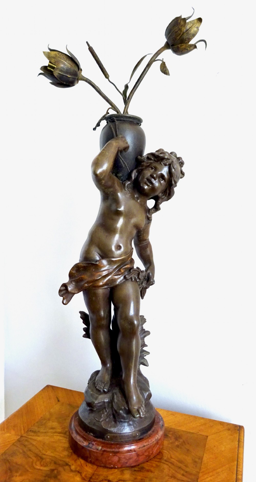 A bronzed spelter table lamp featuring a sculpted cherub figure holding a urn, with floral stem lights mounted on a round marble base.