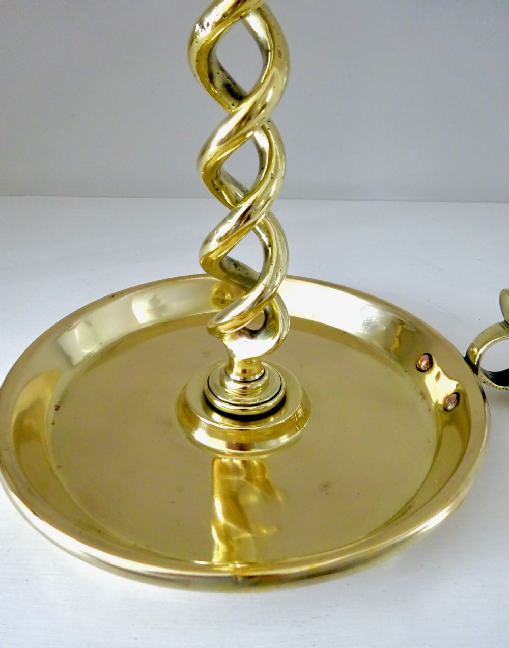A polished brass candlestick featuring an open spiral twisted stem mounted onto a circular saucer base with a side thumb piece. View III
