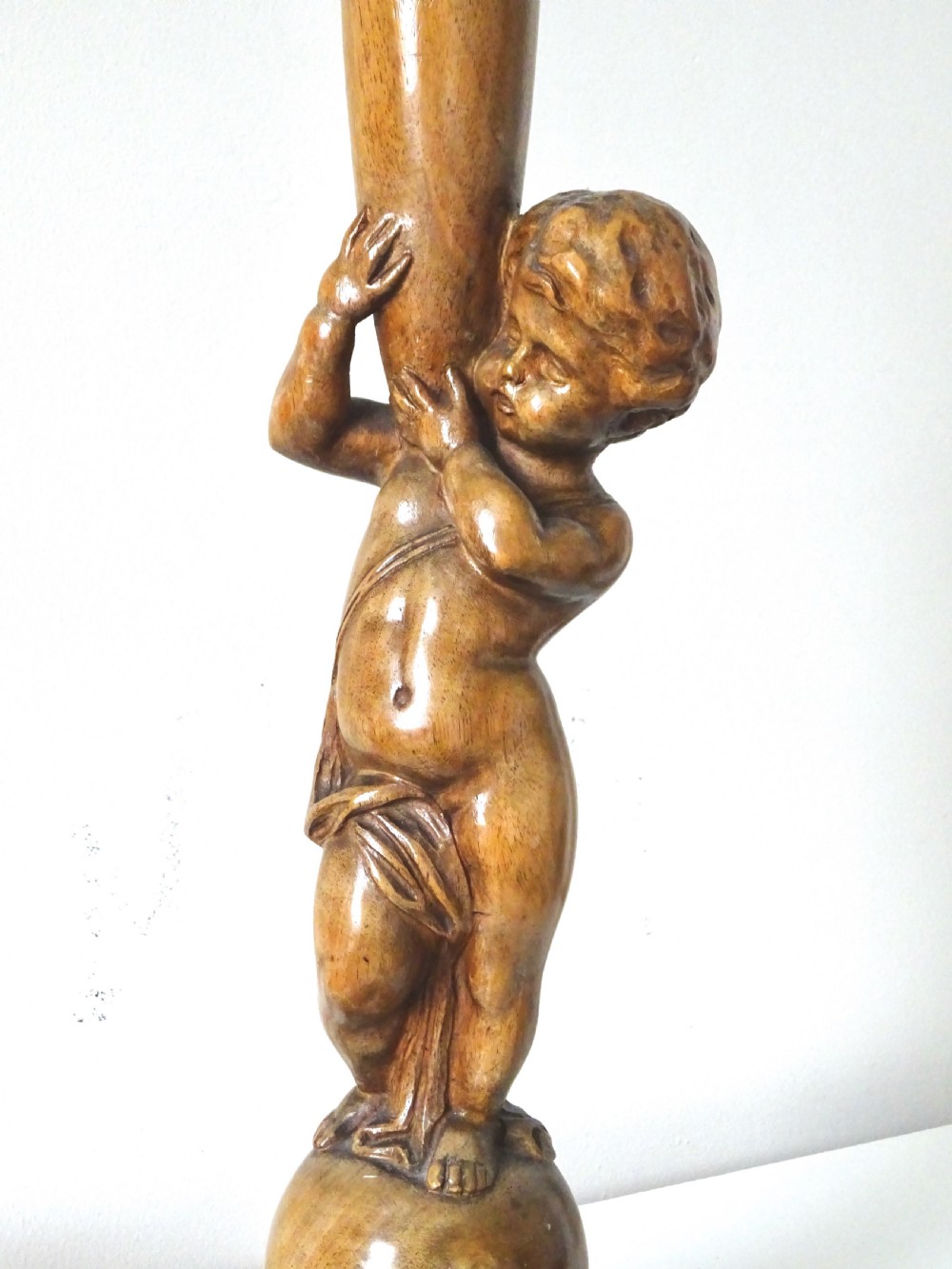 A hand-carved oak table lamp featuring a cherub figure standing on an orb base and holding a fluted stem, topped with a neutral fabric shade. View II