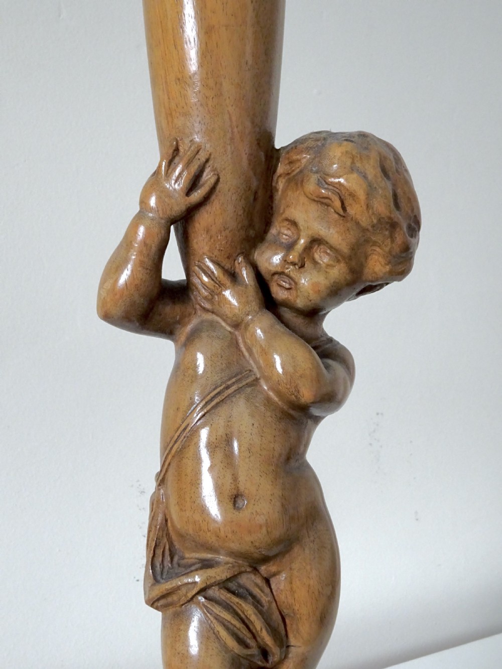A hand-carved oak table lamp featuring a cherub figure standing on an orb base and holding a fluted stem, topped with a neutral fabric shade. View V
