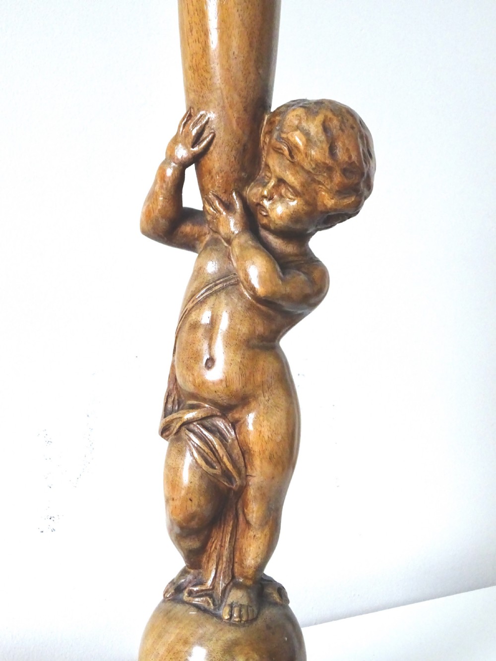 A hand-carved oak table lamp featuring a cherub figure standing on an orb base and holding a fluted stem, topped with a neutral fabric shade. View VII