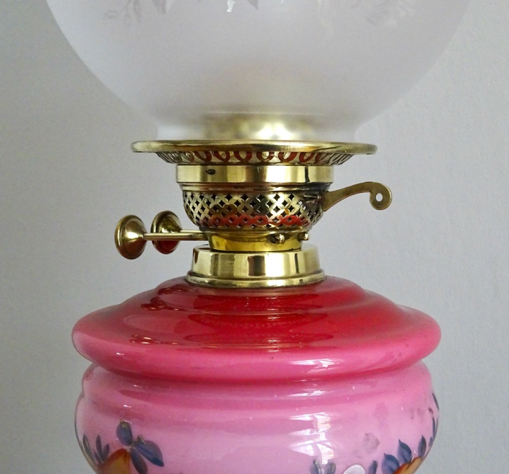 An early twentieth-century brass oil lamp featuring a pink hand-painted glass reservoir, an etched floral glass globe shade, a clear glass chimney, and a black stepped base. View V