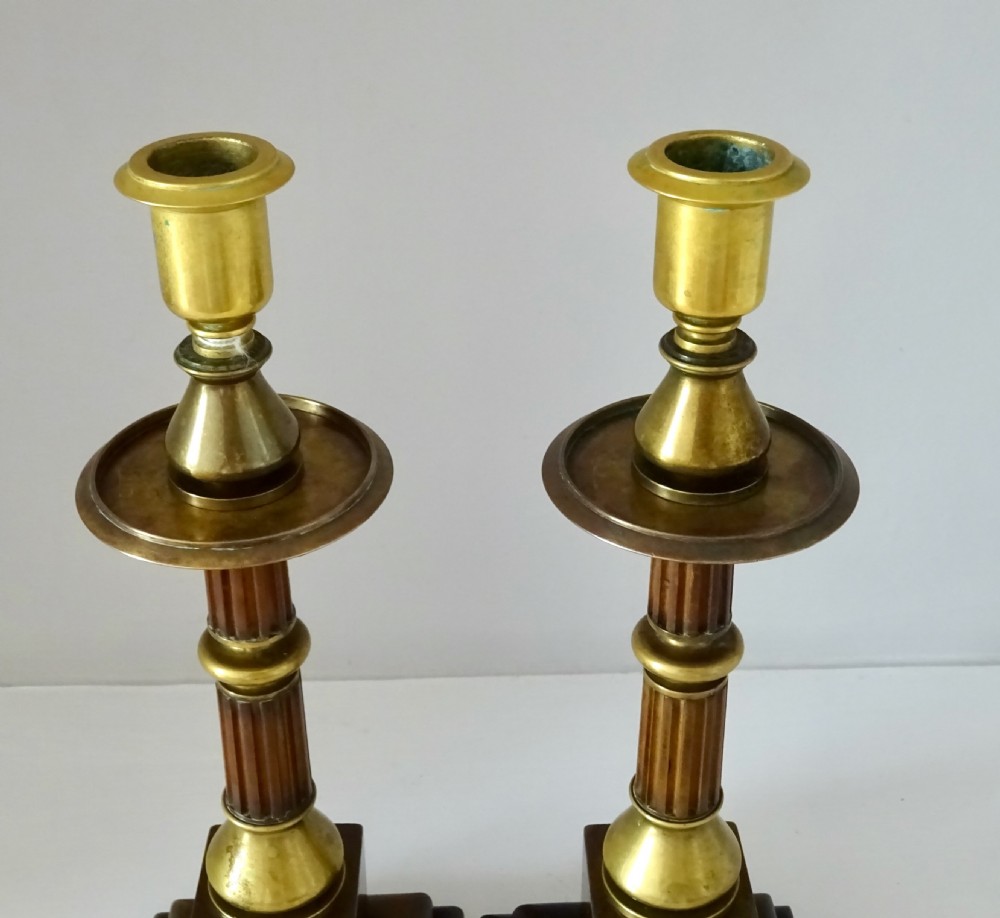 A pair of Edwardian bronze and brass candlesticks featuring fluted shafts, turned sconces, and stepped square bases. View II