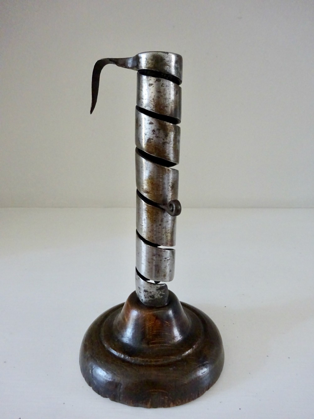 An antique 19th-century iron spiral candlestick with a top hanging hook and internal slider, set into a turned dark wood base. View III