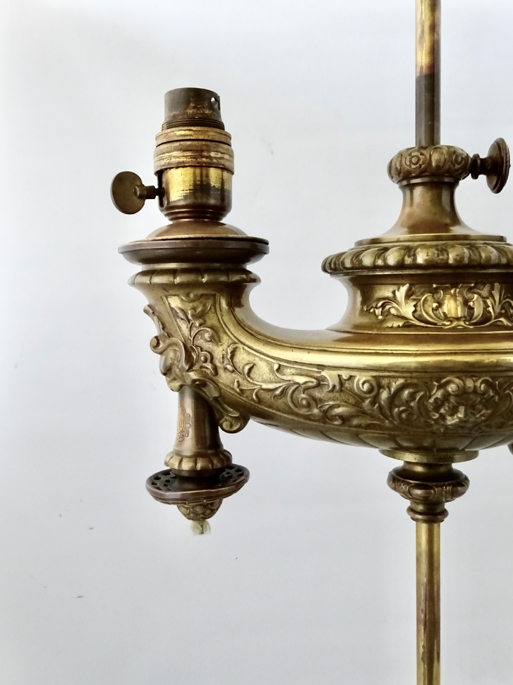 An ornate late Victorian brass oil lamp featuring a weighted circular base, central stem, detailed reservoir with relief carving, and a top carrying ring handle. View II