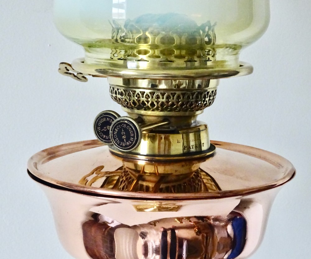 An Arts and Crafts oil lamp featuring a square brass base, a slender turned column stem, a polished copper reservoir, and a pale yellow frilled vaseline glass shade. View II