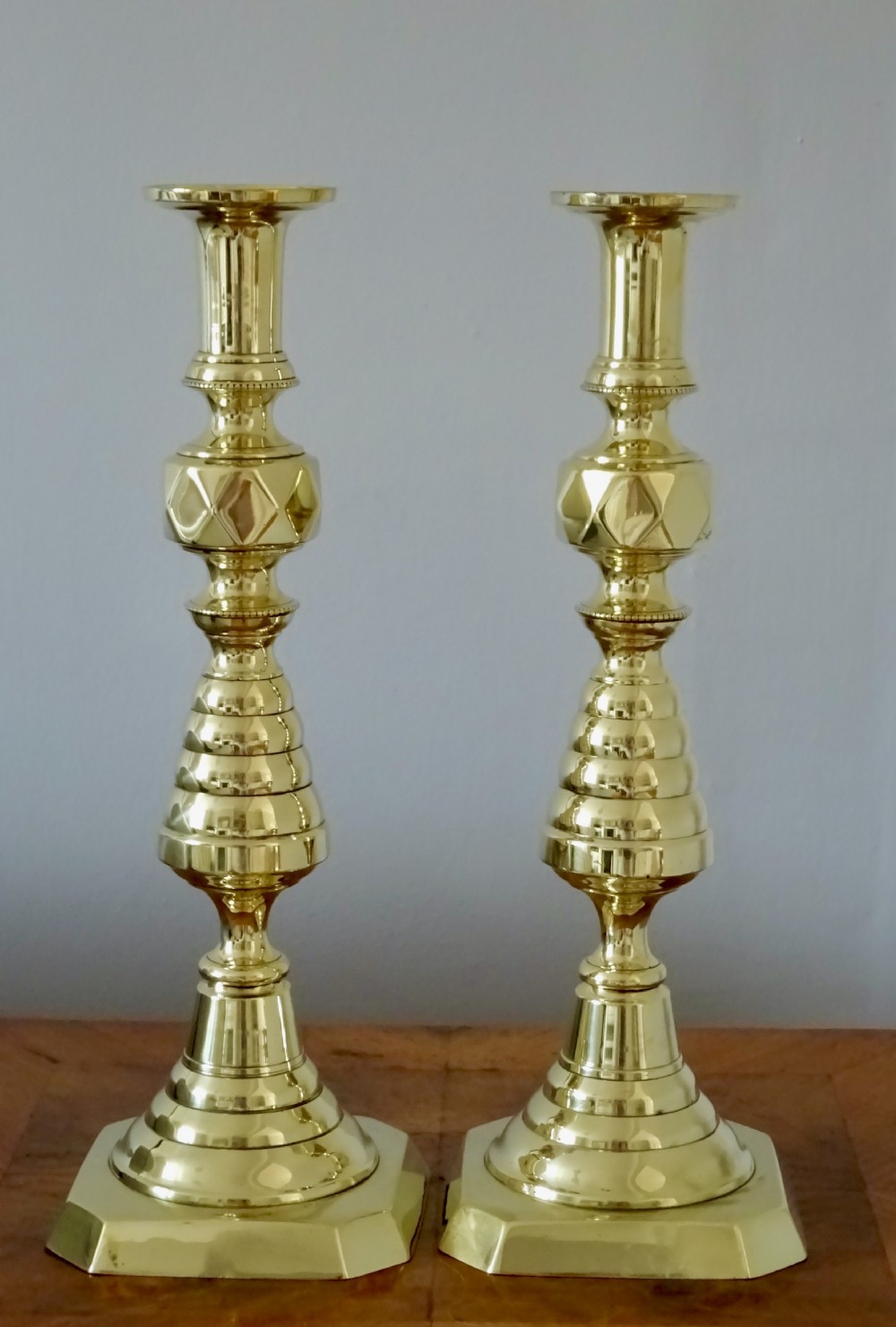 A pair of tall turned brass candlesticks featuring beehive stems, diamond knops, and square bases with canted corners. View VI