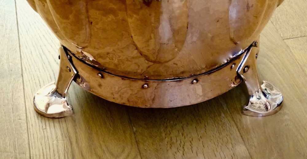 A polished hand-hammered copper log bin featuring a fitted lid with a central finial, repousse lobed sides, side handles, and decorative tripod feet. View V
