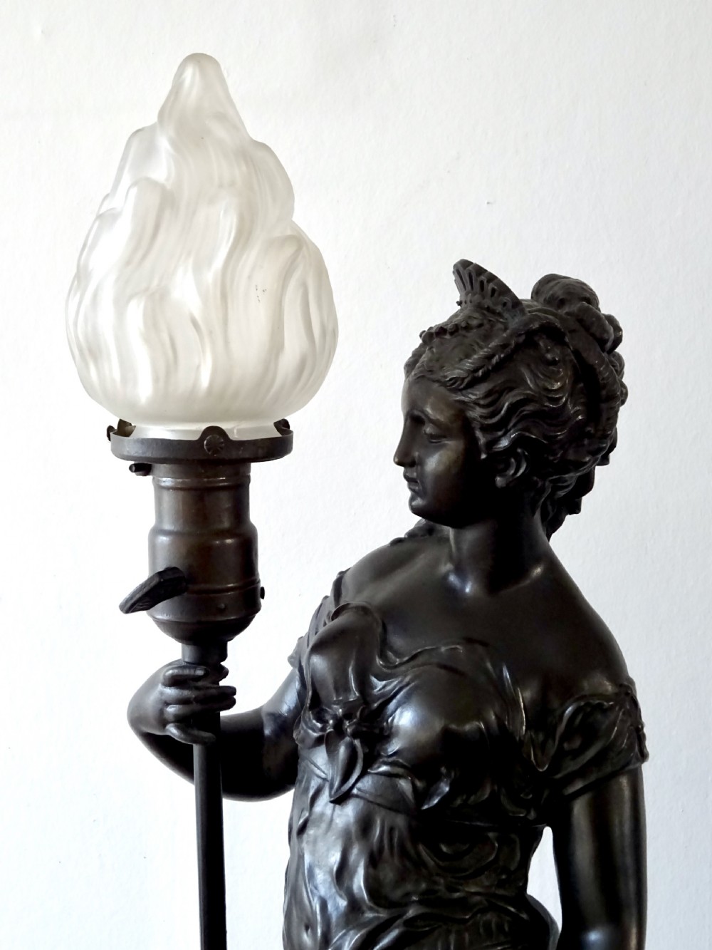 A dark bronze spelter table lamp featuring a classical draped female figure holding a staff topped with a frosted flame glass shade. View III