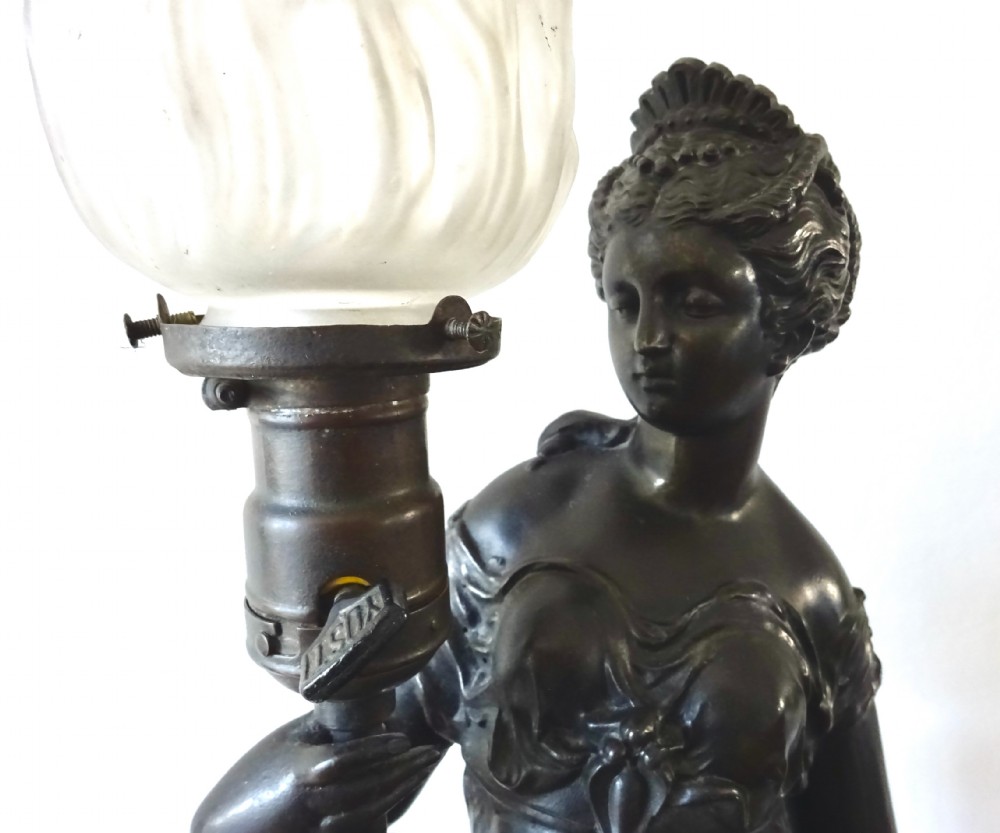 A dark bronze spelter table lamp featuring a classical draped female figure holding a staff topped with a frosted flame glass shade. View IV