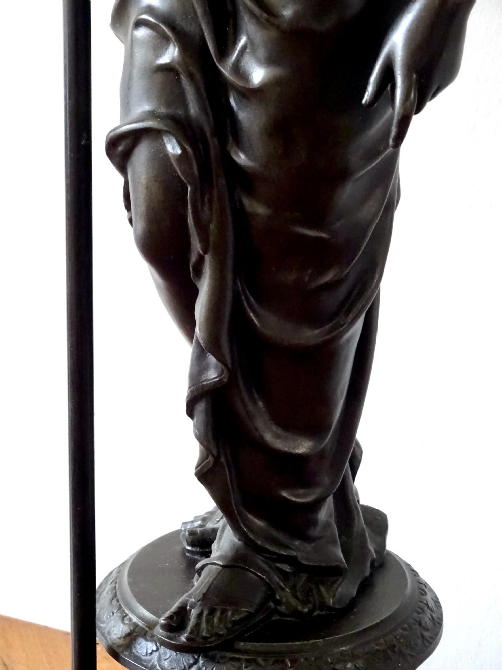A dark bronze spelter table lamp featuring a classical draped female figure holding a staff topped with a frosted flame glass shade. View X