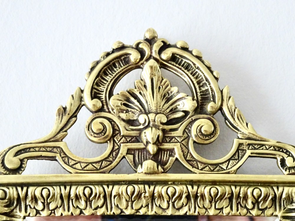 An ornate rectangular cast bronze wall mirror featuring a bevelled glass plate, classical scroll cresting, embossed repeating frame pattern, and a mask apron at the bottom. View III
