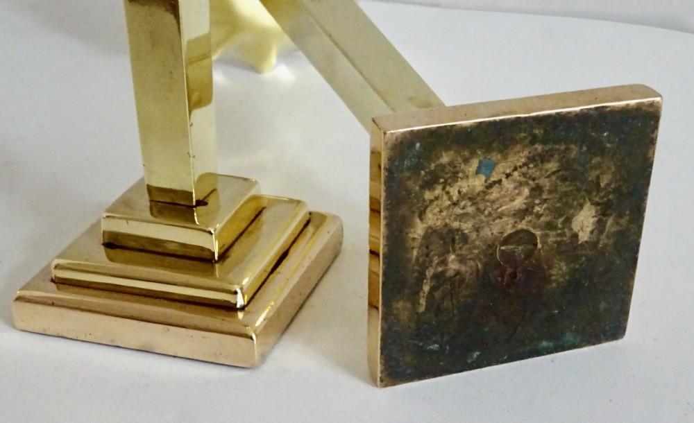 A pair of polished brass candlesticks with stepped square bases, tall central columns, and scalloped drip trays. View IV