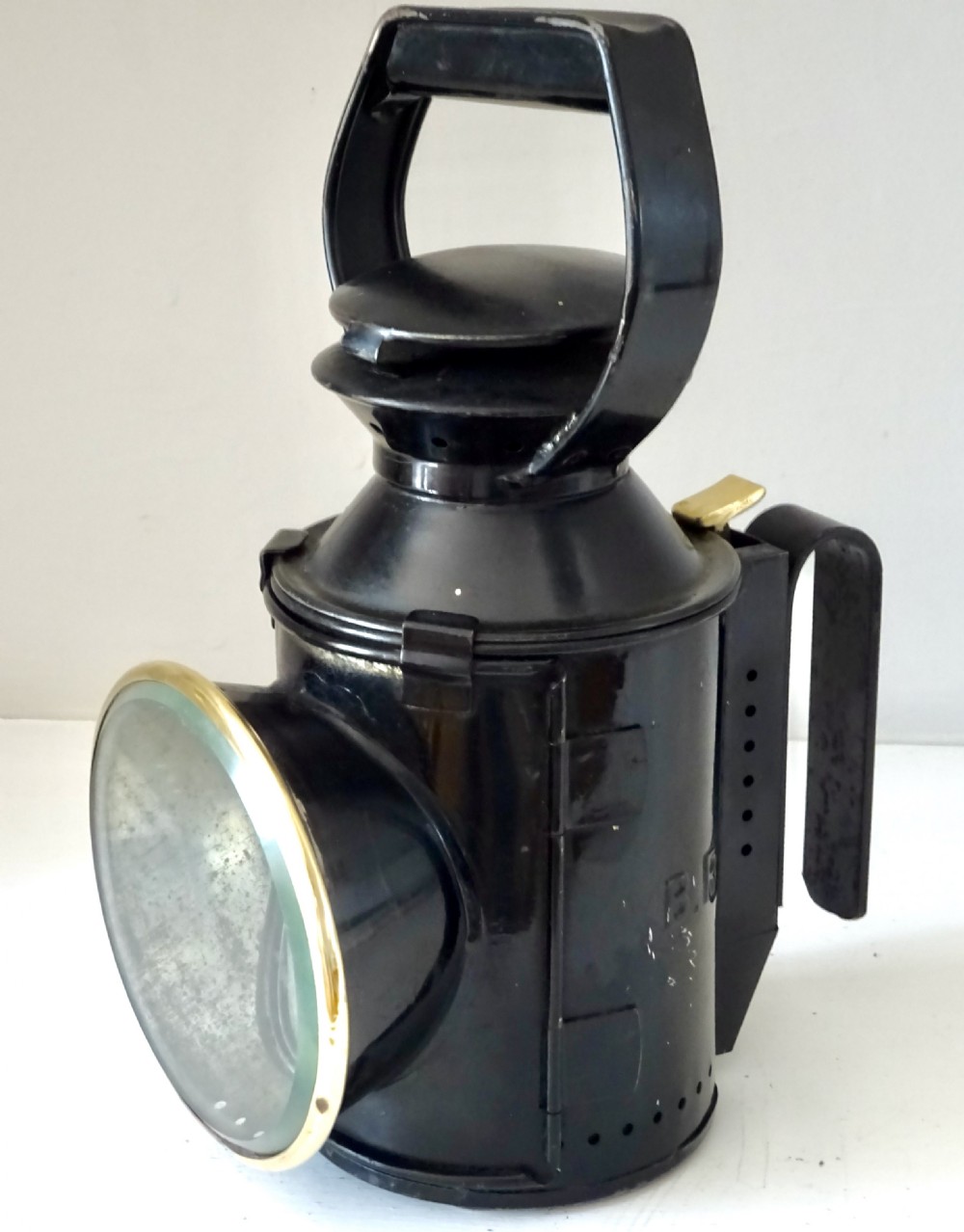 A black painted steel British railway signal oil lamp featuring a brass-rimmed glass lens, carrying handle, and side bracket.
