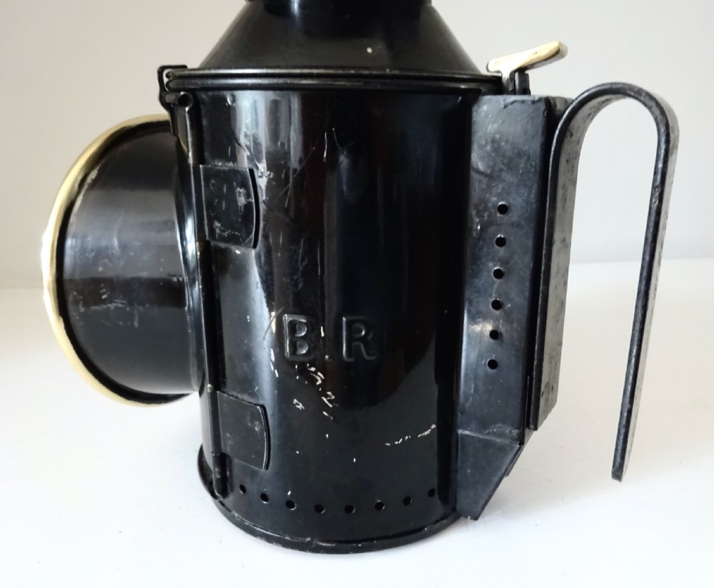 A black painted steel British railway signal oil lamp featuring a brass-rimmed glass lens, carrying handle, and side bracket. View VI