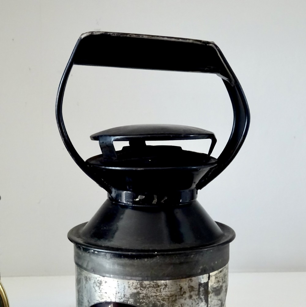 A black painted steel British railway signal oil lamp featuring a brass-rimmed glass lens, carrying handle, and side bracket. View VII