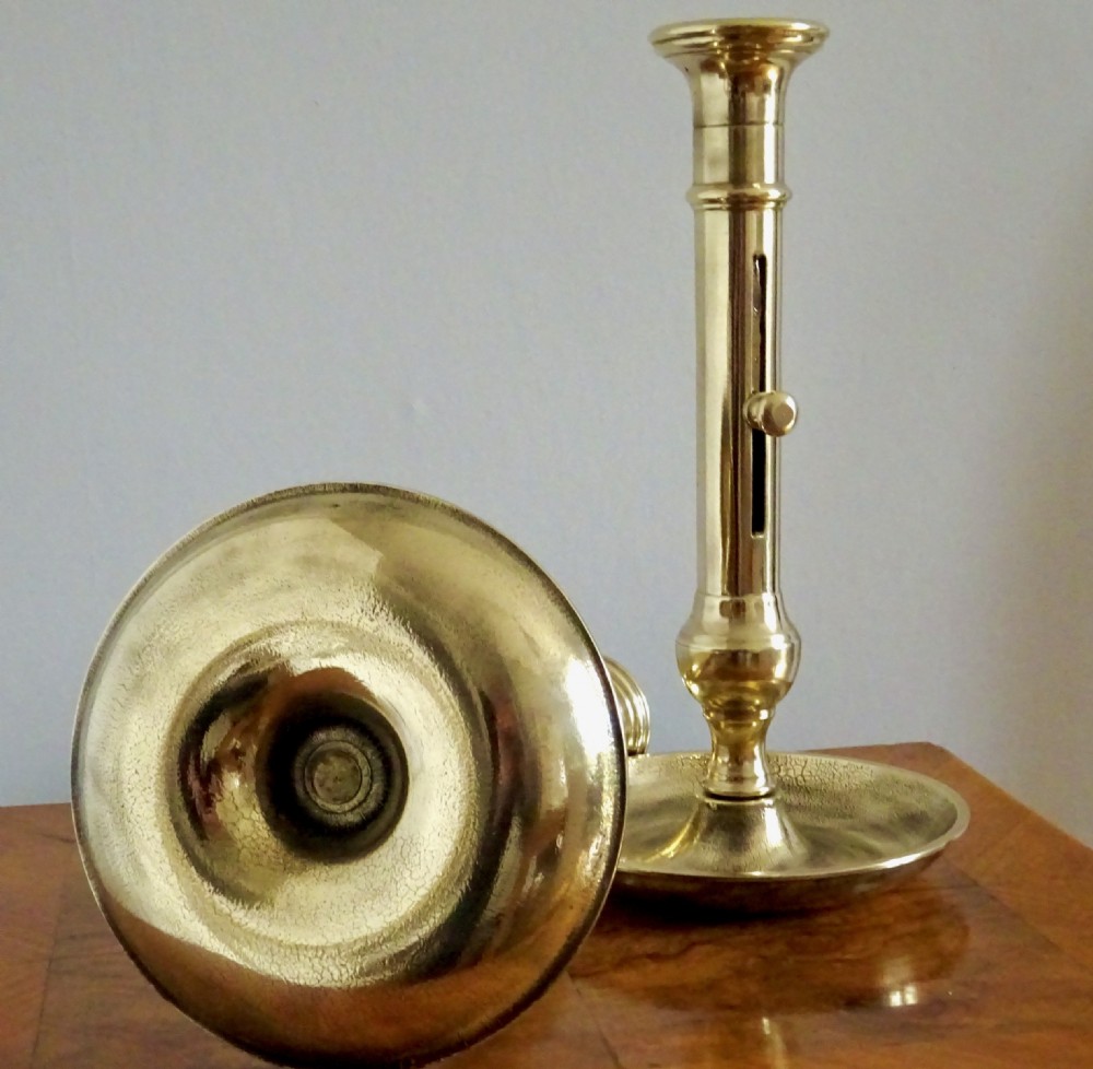 A pair of late Victorian polished brass ejector candlesticks featuring turned stems, side slider knobs, and wide dished bases. View III