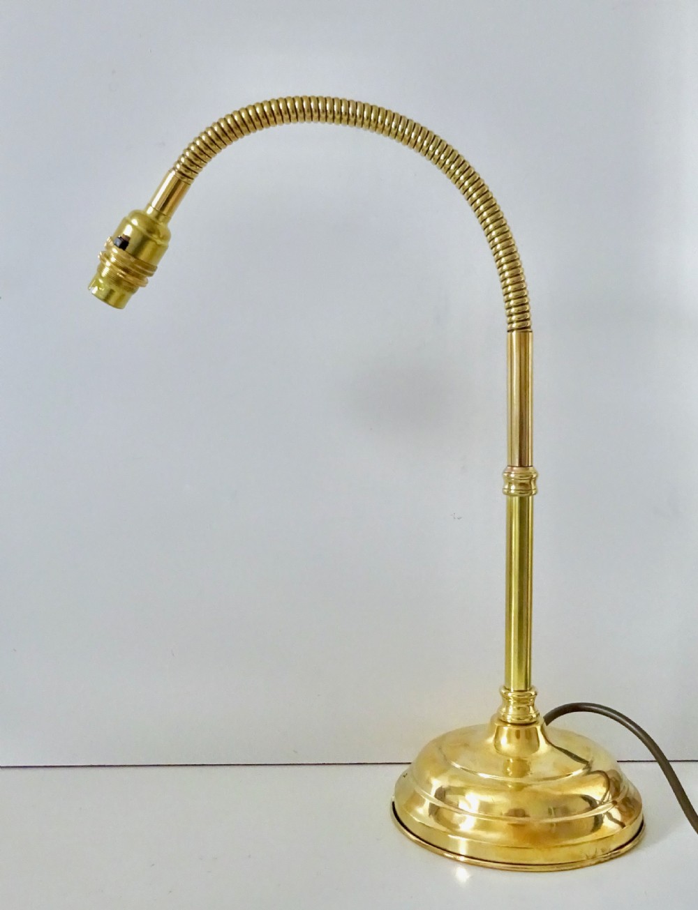 An antique polished brass task lamp featuring a heavy stepped circular base, a flexible gooseneck arm, and a brass bulb socket.