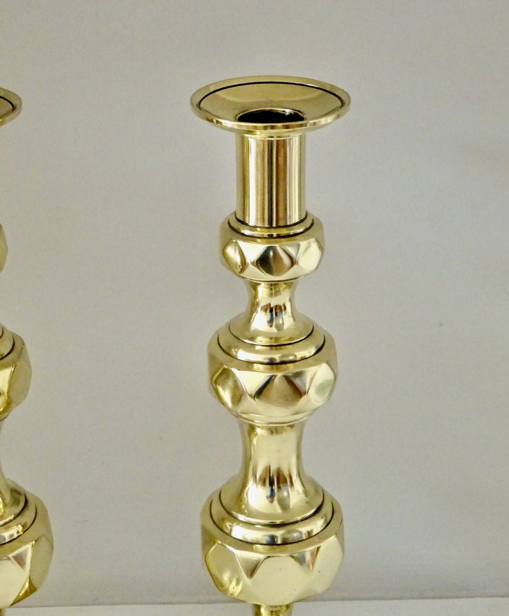 A pair of polished brass Victorian candlesticks featuring faceted knopped stems and square bases. View II