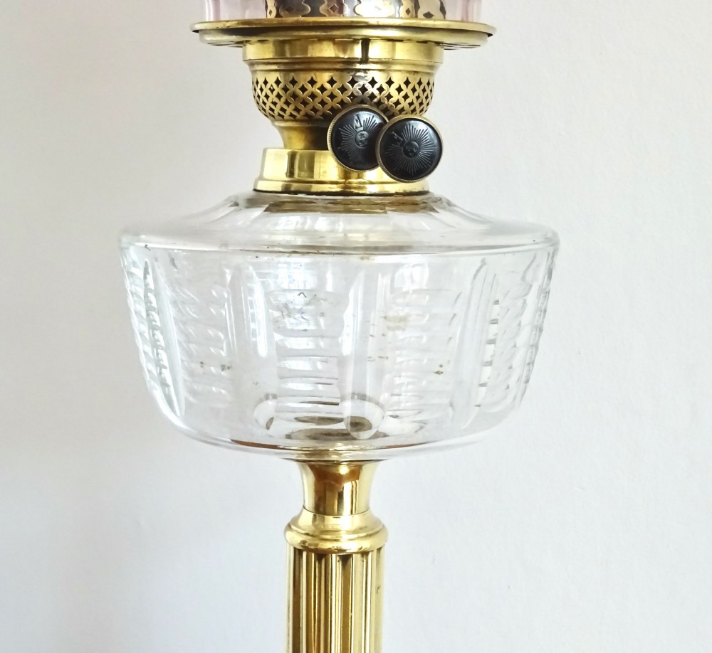 An antique brass column oil lamp with a clear glass reservoir, brass burner, clear glass chimney, and a fluted cranberry glass shade. View V