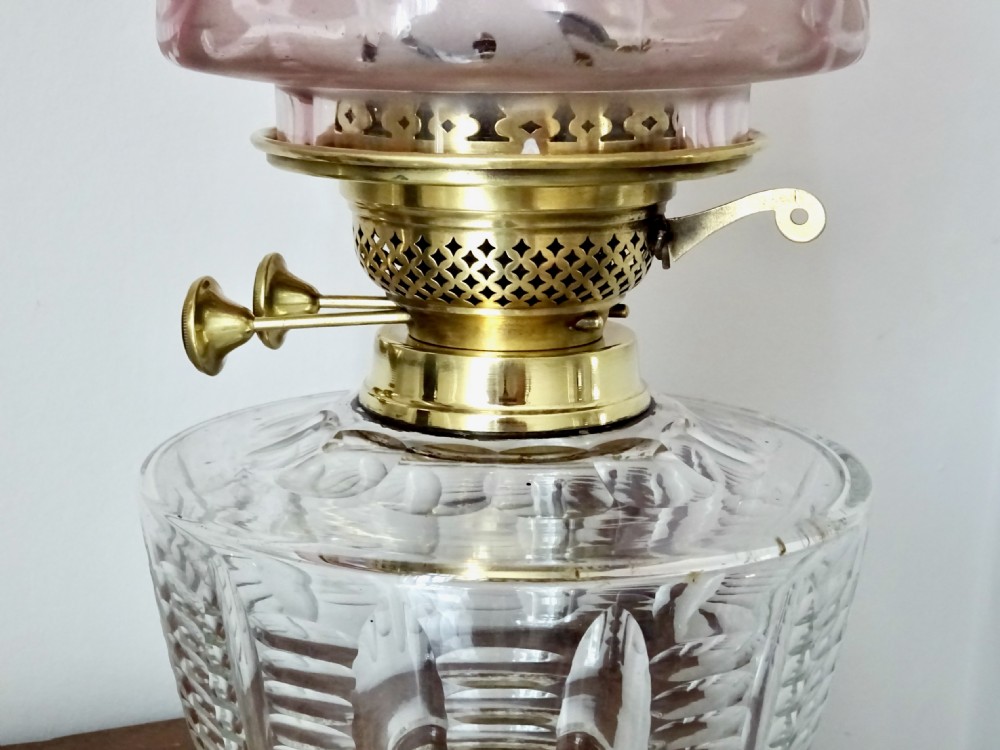 An antique brass column oil lamp with a clear glass reservoir, brass burner, clear glass chimney, and a fluted cranberry glass shade. View IX