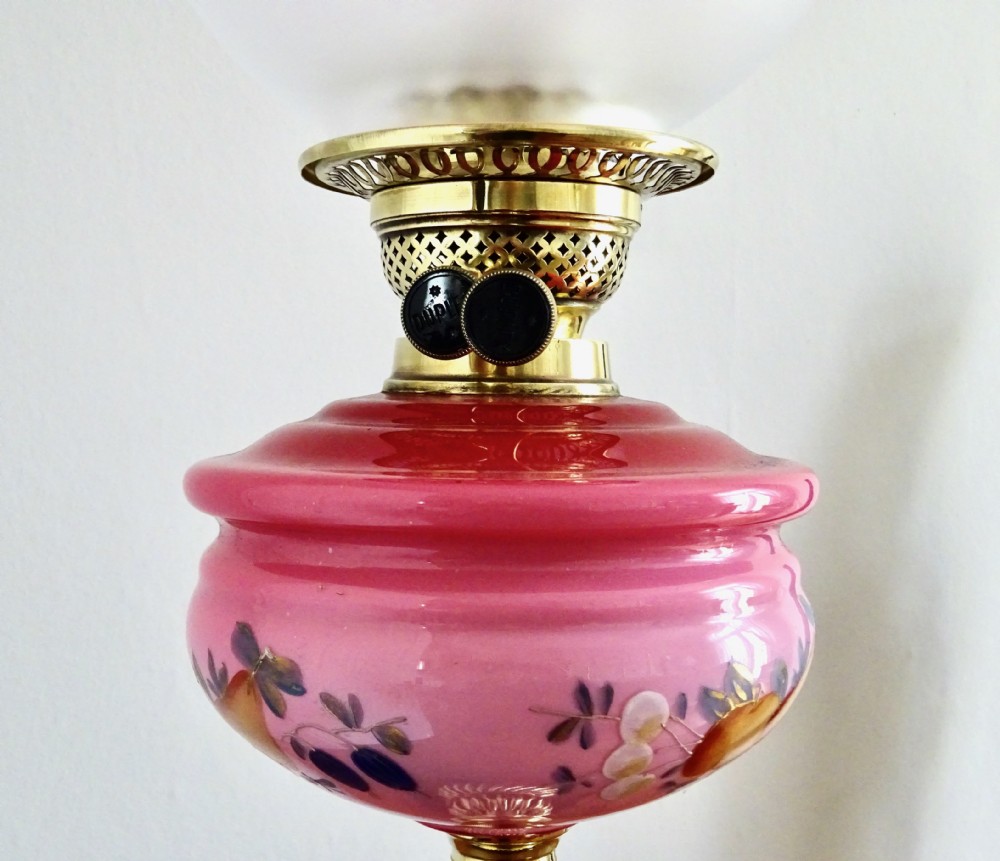 An early twentieth-century brass oil lamp featuring a pink hand-painted glass reservoir, an etched floral glass globe shade, a clear glass chimney, and a black stepped base. View IX