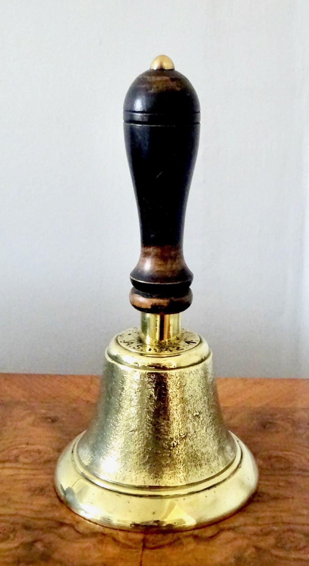 A cast brass hand bell featuring a turned dark wood handle and stamped military markings dated 1942.