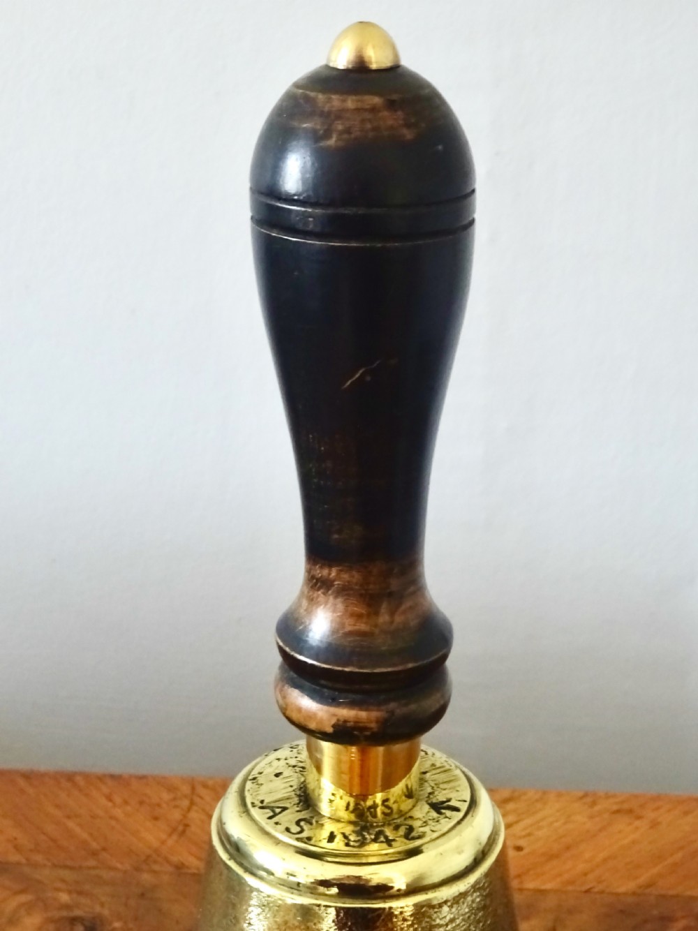 A cast brass hand bell featuring a turned dark wood handle and stamped military markings dated 1942. View II
