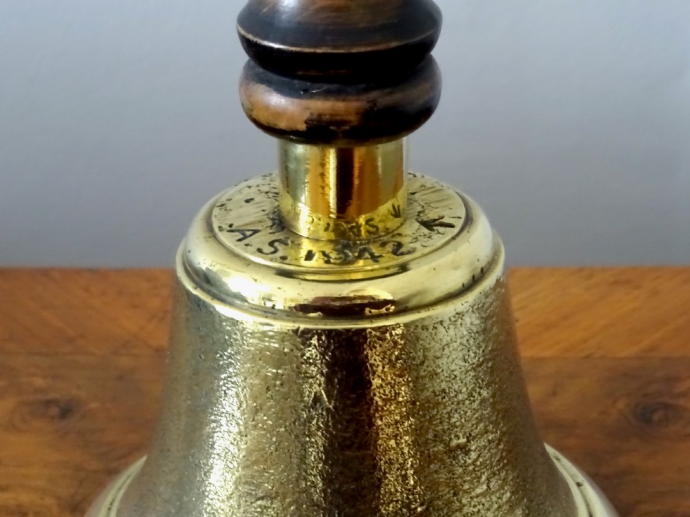 A cast brass hand bell featuring a turned dark wood handle and stamped military markings dated 1942. View IV